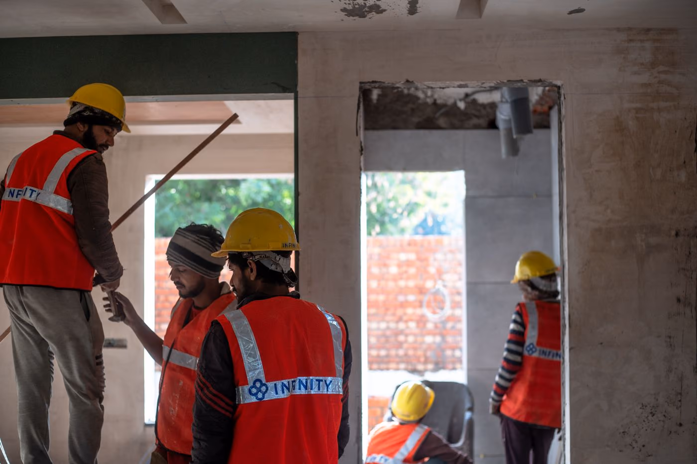 Equipe de obra com capacete e colete refletivo trabalhando dentro de uma edificação em construção.